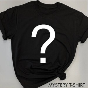 K&ouml;nnte beinhalten: Schwarzes T-Shirt mit einem gro&szlig;en wei&szlig;en Fragezeichen auf der Vorderseite. Der Text "MYSTERY T-SHIRT" ist unten im Bild in Wei&szlig; gedruckt. Das T-Shirt hat kurze &Auml;rmel und einen Rundhalsausschnitt.
