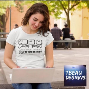 May include: White t-shirt with the words "Ctrl Alt Del" above the text "Control yourself, alter your thinking, delete negativity" in black. The shirt is being worn by a person using a laptop.