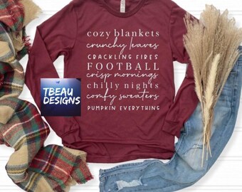 May include: A long-sleeve maroon shirt featuring white text that reads: cozy blankets, crunchy leaves, crackling fires, FOOTBALL, crisp mornings, chilly nights, comfy sweaters, PUMPKIN EVERYTHING. A TBEAU DESIGNS logo is visible on the left side.