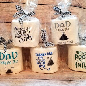 May include: Several rolls of toilet paper are wrapped in cellophane and tied with black and white checkered bows. Each roll has a different humorous message about fathers, including "World's Greatest Farter Father" and "You're the Poo-fect Father."