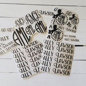 Op de afbeelding: Een verzameling gepersonaliseerde stickers met de naam "Ally Lawson" en de initialen "AML" in verschillende lettertypen en ontwerpen. Sommige stickers bevatten een eenhoornsilhouet. De stickers zijn zwart en wit.
