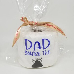 May include: A white toilet paper roll with the blue text "DAD you're the" and a black poop graphic. The roll is wrapped in clear cellophane and tied with a ribbon that says "Merry Christmas".