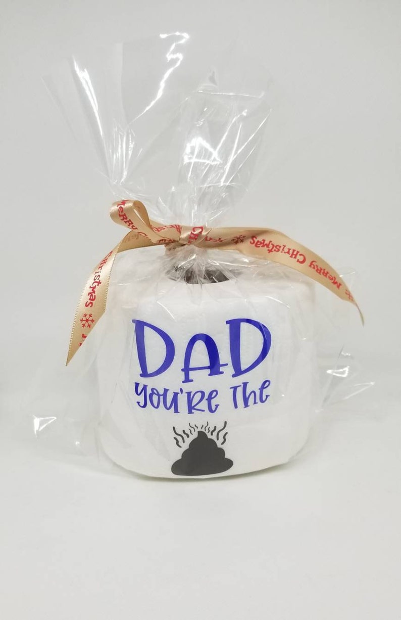 May include: A white toilet paper roll with the blue text "DAD you're the" and a black poop graphic. The roll is wrapped in clear cellophane and tied with a ribbon that says "Merry Christmas".