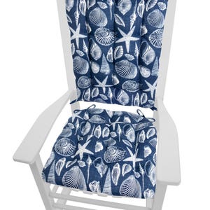 Op de afbeelding: Een witte houten schommelstoel met marineblauwe kussens. De kussens hebben een wit patroon van schelpen en zeesterren. De stoel is ontworpen voor gebruik buitenshuis en biedt comfortabele zitplaatsen voor een veranda of terras.
