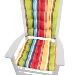 Op de afbeelding: Witte houten Adirondack stoel met kleurrijke gestreepte kussens. De kussens hebben verticale strepen in groen, rood, geel, blauw en wit. De stoel is ontworpen voor gebruik buitenshuis.