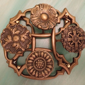 May include: A gold-toned metal decorative piece with four ornate, circular designs. The piece has a geometric, openwork design with small gold beads around the edges.