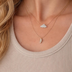 May include: Two delicate gold necklaces. The top necklace features a cloud-shaped pendant, and the bottom necklace has a rectangular pendant with small, sparkling accents. The necklaces are worn on a person.