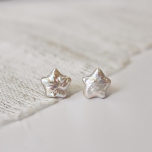 Peut inclure: Une paire de boucles d'oreilles en forme d'étoile en perles. Les boucles d'oreilles sont de couleur blanc irisé clair et ont une forme légèrement irrégulière.