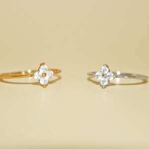 May include: Two dainty rings with a four-leaf clover design set with clear cubic zirconia stones. One ring is gold and the other is silver.