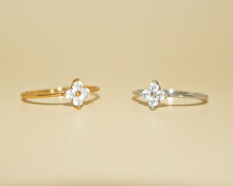 May include: Two dainty rings with a four-leaf clover design set with clear cubic zirconia stones. One ring is gold and the other is silver.