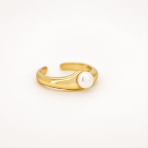 May include: A gold ring with a single white pearl set in the center. The ring is simple and elegant.
