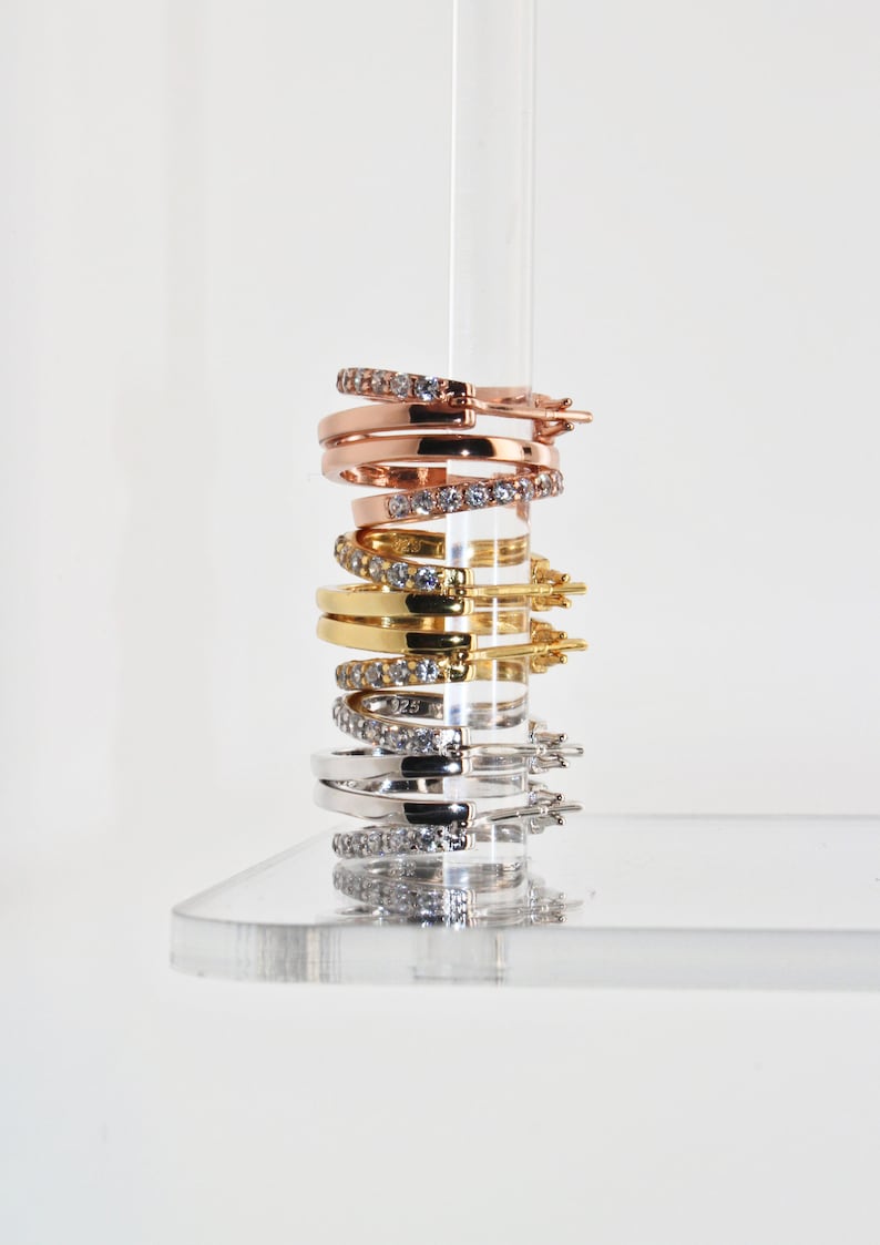 K&ouml;nnte beinhalten: Ein Stapel von vier Creolen mit Zirkonia-Steinen. Die Ohrringe sind in verschiedenen Metalloberfl&auml;chen: Ros&eacute;gold, Gold und Silber.