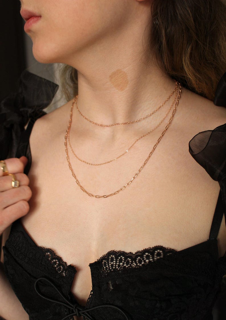 May include: A woman wearing a black lace top with a gold chain necklace layered on top of another gold chain necklace.