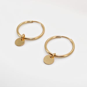 May include: Gold hoop earrings with a small round charm hanging from each hoop.