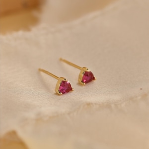 Può includere: Un paio di orecchini a lobo in oro con pietre preziose triangolari di colore rosa vivace. Ogni orecchino è dotato di un sottile perno in oro e di una chiusura sicura, caratterizzato da un design essenziale con finitura in metallo lucido.