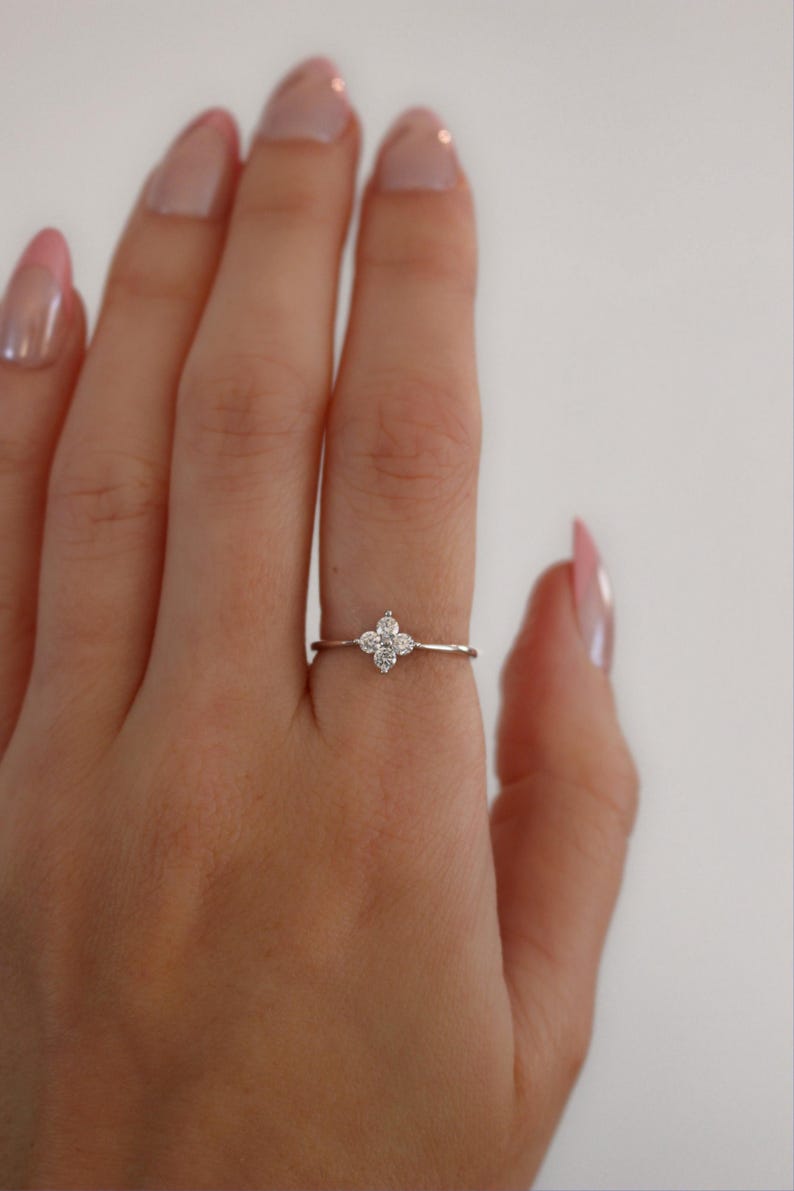 May include: A delicate silver ring with a small, four-leaf clover design set with clear sparkling stones.