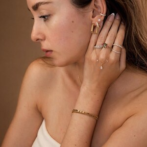 May include: A collection of gold jewelry, including earrings, rings, a bracelet, and a necklace with a pendant. The earrings are rectangular, and the rings feature gemstones and diamonds. The bracelet is a chain style.