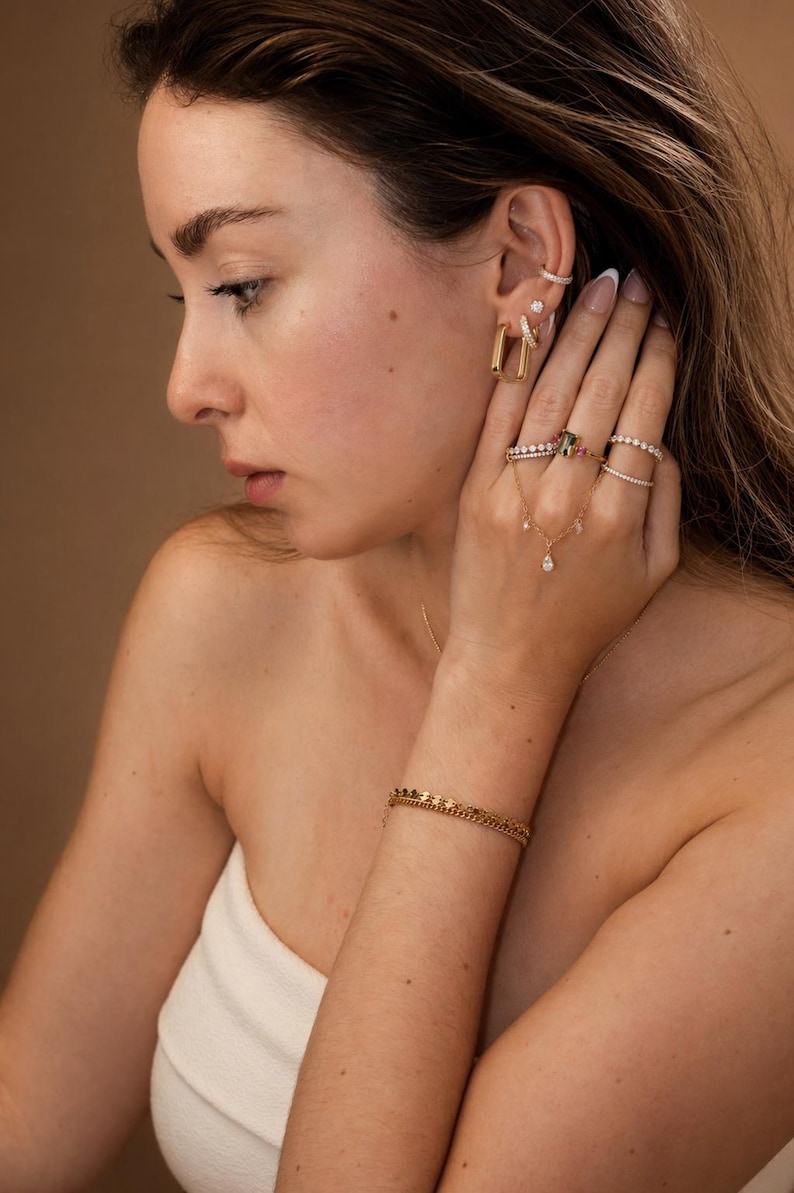 May include: A collection of gold jewelry, including earrings, rings, a bracelet, and a necklace with a pendant. The earrings are rectangular, and the rings feature gemstones and diamonds. The bracelet is a chain style.