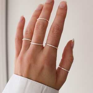 May include: A hand wearing multiple thin silver rings on different fingers.