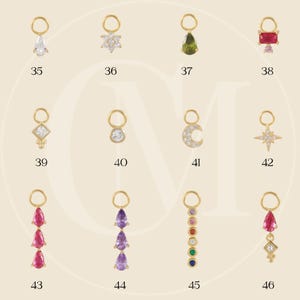 May include: A collection of gold-toned charms with various gemstone and crystal designs. The charms include teardrop, starburst, and floral shapes, as well as a crescent moon and a series of colorful gems. Each charm has a small loop for attachment.