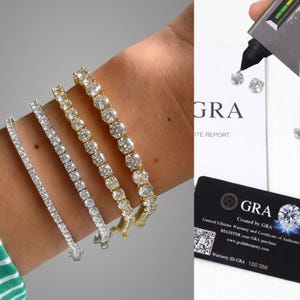 May include: Four tennis bracelets featuring round-cut stones in silver and gold-toned settings. A diamond tester is shown touching a loose stone above a GRA report and a black GRA authenticity card with a QR code and the text GRA Created by GRA.