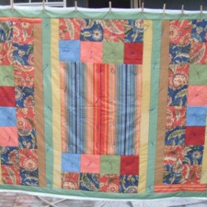 May include: A quilt with a patchwork design featuring various colors and patterns, including red, blue, green, and brown. The quilt is made up of squares and rectangles, and the fabric is a mix of floral and geometric prints.