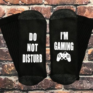 May include: A pair of black socks with white text. One sock says "Do Not Disturb" and the other says "I'm Gaming" with a white video game controller graphic.