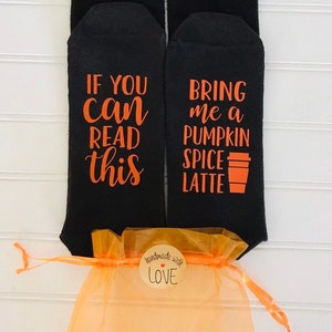 May include: A pair of black socks with orange text. One sock says "If you can read this" and the other sock says "Bring me a pumpkin spice latte". The socks are packaged in a light orange drawstring bag with a small brown tag that says "Handmade with love".