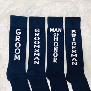 May include: Four pairs of dark blue socks with white text. The socks read "Groom", "Groomsman", "Man of Honor", and "Bridesman".