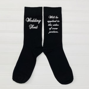 May include: A pair of black socks with white text. The text on one sock reads "Wedding Font". The text on the other sock reads "Will be applied to the sides of crew portion."