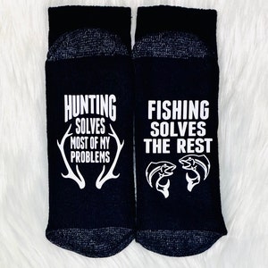 May include: A pair of black socks with white text. One sock says "Hunting solves most of my problems" with a pair of antlers. The other sock says "Fishing solves the rest" with two fish.