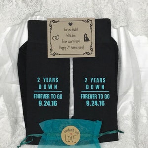 May include: Two black socks with the text "2 Years Down Forever To Go 9.24.16" in turquoise blue. The socks are packaged in a turquoise blue organza bag with a brown tag that says "handmade with love". A card with the text "For my Bride! With love From your Groom! Happy 2nd Anniversary!" is included.