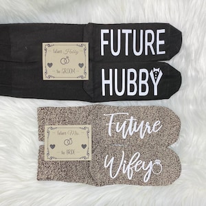 Puede incluir: Dos pares de calcetines con texto impreso. Un par es negro con el texto "FUTURE HUBBY" y el otro par es marrón con el texto "Future Wifey".