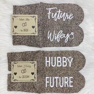 May include: A pair of brown socks with white text. One sock says "Future Wife" with a ring symbol. The other sock says "Hubby Future". The socks are accompanied by two small cards with the text "Future Mrs. the Bride" and "Future Hubby the Groom".