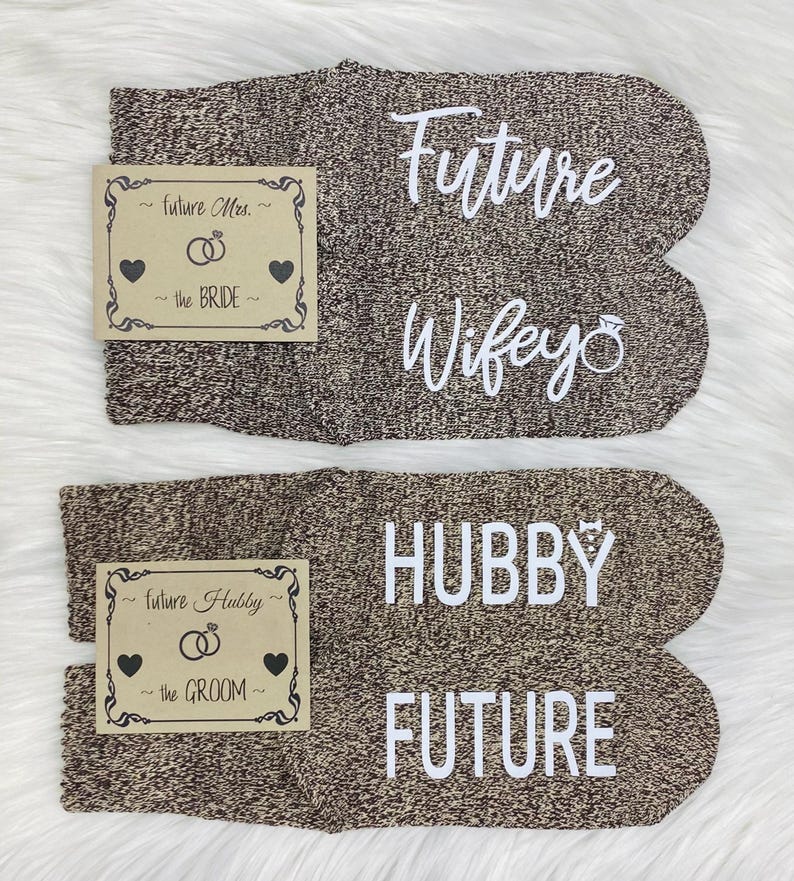 May include: A pair of brown socks with white text. One sock says "Future Wife" with a ring symbol. The other sock says "Hubby Future". The socks are accompanied by two small cards with the text "Future Mrs. the Bride" and "Future Hubby the Groom".