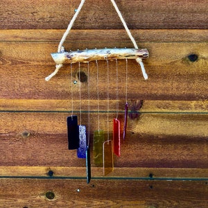 May include: A handcrafted wind chime featuring a natural wood branch, suspended by a rope, with colorful glass rectangles hanging below. The glass pieces are in shades of blue, purple, yellow, orange, and red.