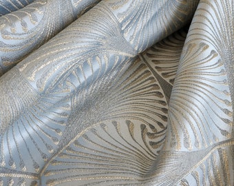 May include: Close-up of a blue and gold fabric with a repeating pattern of stylized leaves. The fabric has a subtle sheen and a textured surface.