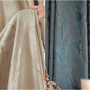 May include: Two fabric swatches with a leaf pattern. The fabric on the left is a light beige color with gold leaf accents. The fabric on the right is a dark blue color with gold leaf accents.