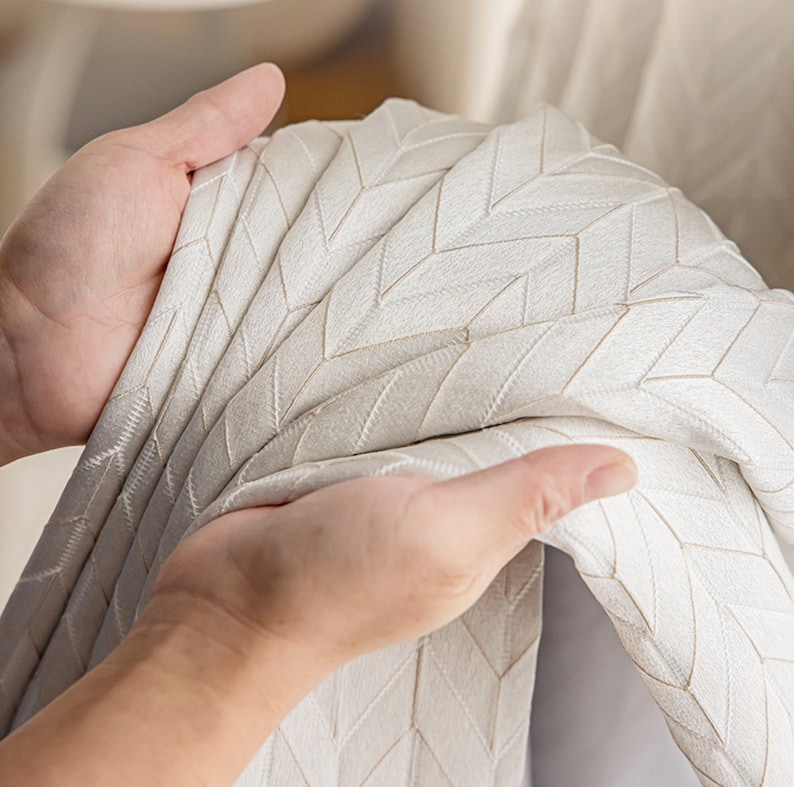 May include: Close-up of a white fabric with a subtle herringbone pattern. The fabric is soft and textured, with a slight sheen.