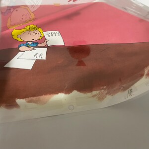 May include: A cartoon illustration of a girl with blonde hair sitting at a desk writing on a piece of paper. The paper has the letters "R.H." written on it. The girl is wearing a blue shirt and a red bow. The desk is brown and the background is pink.