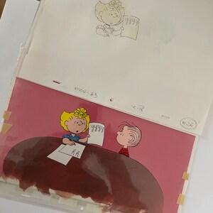 May include: A pink background with a brown table. Two cartoon characters are sitting at the table. One character is a girl with blonde hair and a blue shirt. The other character is a boy with brown hair and a red shirt. The girl is holding a piece of paper with the word "YYYYY" written on it. The boy is looking at the girl. The text "R.H." is written on the table.