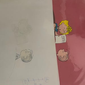 May include: A pink background with a black and white cartoon drawing of a girl with blonde hair and a blue dress. The girl is holding a piece of paper with the word "remarkable" written on it. The drawing is on a clear sheet of paper.