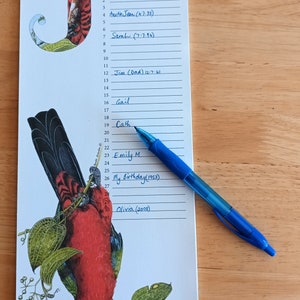K&ouml;nnte beinhalten: Ein wei&szlig;er Kalender mit dem Monat Juli darauf gedruckt. Der Kalender hat eine rote und gr&uuml;ne Vogel-Illustration auf der linken Seite. Die Daten sind von 1 bis 31 nummeriert. Auf dem Kalender sind Namen und Daten in blauer Tinte geschrieben.