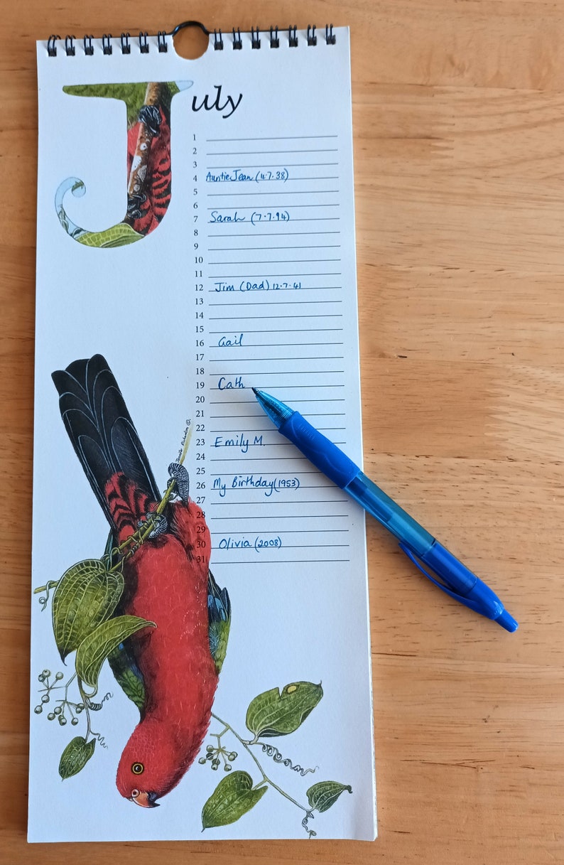 K&ouml;nnte beinhalten: Ein wei&szlig;er Kalender mit dem Monat Juli darauf gedruckt. Der Kalender hat eine rote und gr&uuml;ne Vogel-Illustration auf der linken Seite. Die Daten sind von 1 bis 31 nummeriert. Auf dem Kalender sind Namen und Daten in blauer Tinte geschrieben.