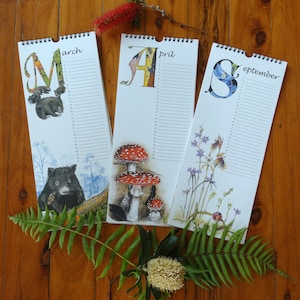 K&ouml;nnte beinhalten: Drei Wandkalender mit bunten Illustrationen von Tieren und Pflanzen. Die Kalender sind f&uuml;r M&auml;rz, April und September. Jeder Kalender hat eine andere Tier- und Pflanzenillustration. Die Kalender befinden sich auf einer Holzoberfl&auml;che.