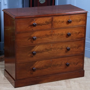 May include: A mahogany chest of drawers with five drawers and dark knobs. The chest has a polished finish, showcasing the wood grain. The drawers are arranged in two rows. A traditional piece of furniture, approximately 120cm wide.