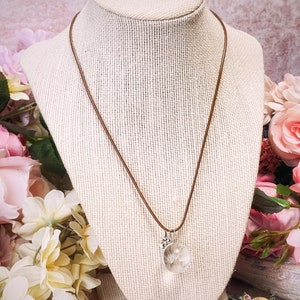 May include: A brown leather cord necklace with a silver pendant featuring a clear glass orb containing a dried dandelion. The pendant has a small silver flower charm attached.