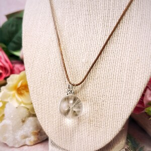 May include: A delicate necklace with a brown cord and a silver pendant featuring a dandelion seed head encased in a clear glass sphere.