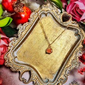 May include: A gold necklace with a small, orange, square pendant on a gold, ornate, decorative tray.