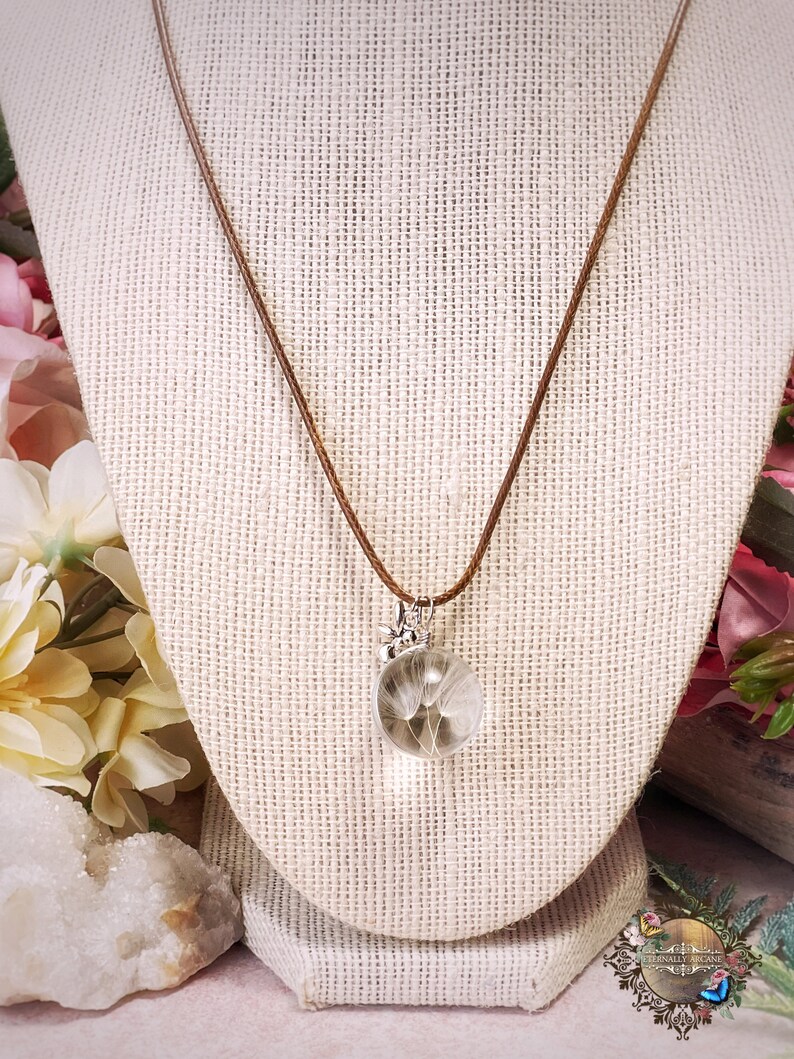 May include: A brown leather cord necklace with a silver pendant featuring a dandelion inside a clear glass orb.